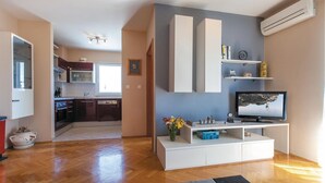 A modern living room with a flat-screen TV, white entertainment unit, and a kitchen in the background.