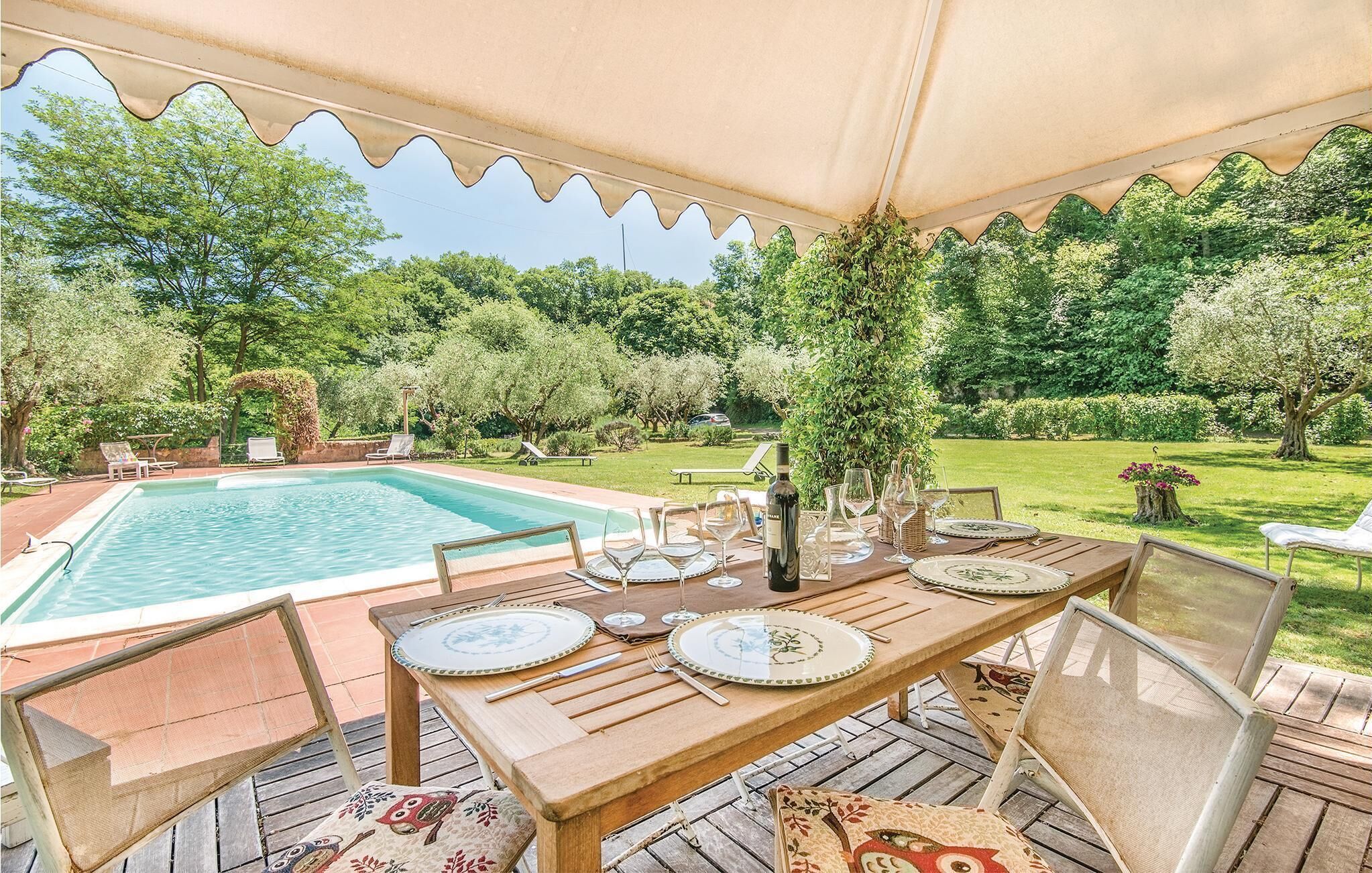 Ein Essbereich im Freien mit Pool, Holztisch und Stühlen, umgeben von üppiger Bepflanzung und Bäumen.