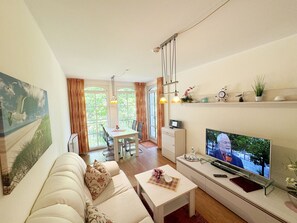 A living room with a sofa, coffee table, TV, and dining area with chairs and a table.