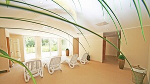 Una habitación iluminada por el sol con tres sillones blancos, un ventanal grande y una planta en maceta.