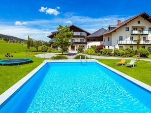 A swimming pool with a clear blue water, surrounded by a well-maintained lawn and a building with balconies.