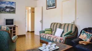Een woonkamer met een bank, fauteuils, een salontafel met kopjes, een televisie op een dressoir en kunstwerken aan de muur.