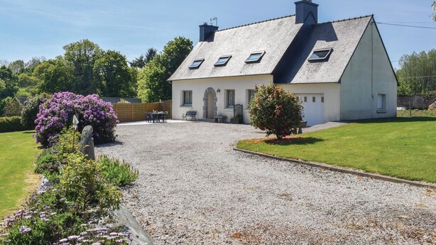 Een tweelaags huis met een grindpad, een gazon en bloeiende struiken.