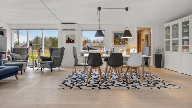 Un salon moderne avec un coin repas, comprenant une grande fenêtre, un tapis à motifs noir et blanc et une table à manger avec des chaises.