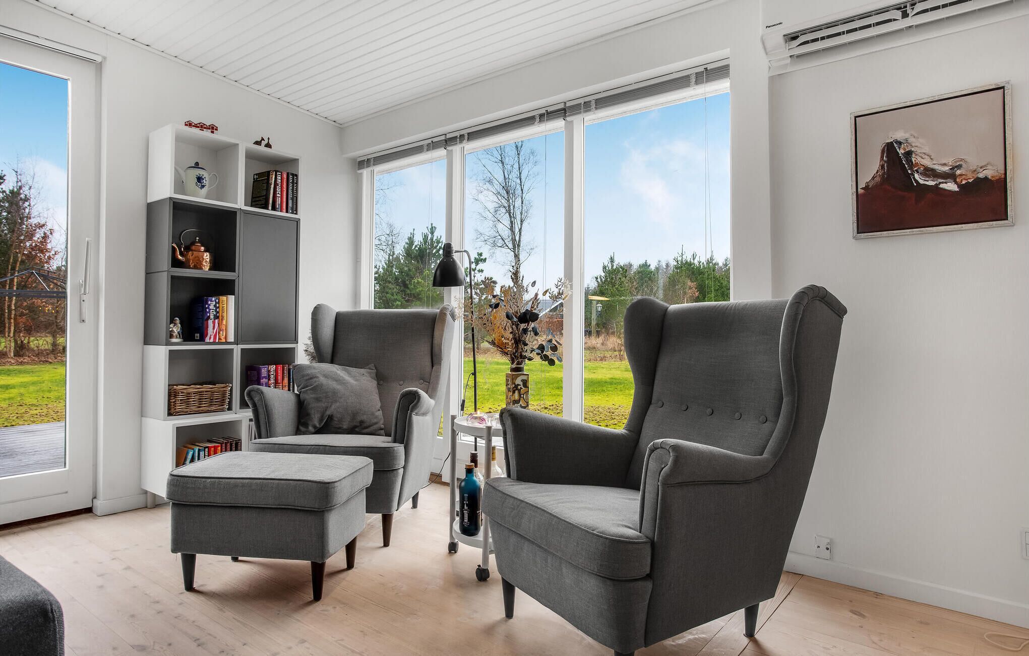 Un salon moderne avec un fauteuil gris, un pouf et une bibliothèque blanche.