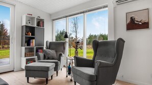 Un salon moderne avec un fauteuil gris, un pouf et une bibliothèque blanche.