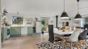 Une cuisine moderne avec des meubles de couleur verte, un coin repas avec une table blanche et des chaises noires, et une grande fenêtre qui laisse entrer la lumière naturelle.