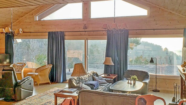 Ein geräumiges Wohnzimmer mit hoher Decke, großen Fenstern und Blick ins Freie.