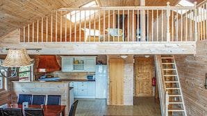 Ein Holzblockhaus-Interieur mit Essbereich, Küche und Schlafzimmer auf dem Dachboden mit Balkon.
