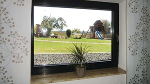 Ramen met uitzicht op een speeltuin, inclusief een glijbaan en schommel, en een bloempot op de vensterbank.