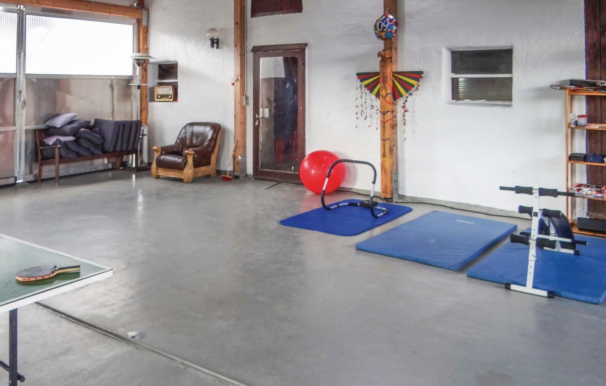 Una habitación amplia con mesa de ping pong, colchonetas de ejercicio, una pelota de gimnasia roja y un saco de boxeo colgante.