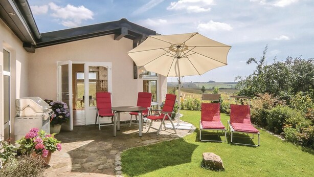 Een terras buiten met een tafel, stoelen, een grote parasol en uitzicht op het landschap.