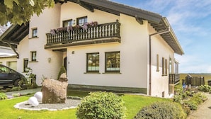 Een tweelaags huis met een balkon, oprit en een verzorgde tuin.