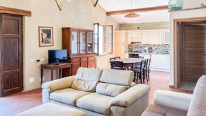Un salon comprenant un canapé, un téléviseur, des meubles en bois et un coin repas avec une table et des chaises.