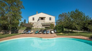 Une maison avec une piscine, entourée d’arbres et dotée d’une terrasse avec des chaises longues.