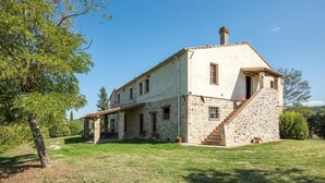 Une maison en pierre à deux étages, dotée d’un porche couvert et d’un escalier menant à l’étage supérieur.