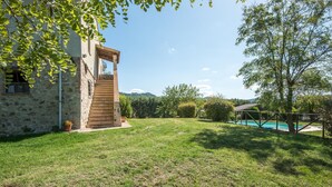 Un bâtiment en pierre avec un escalier en bois menant à un balcon, entouré d’une pelouse verdoyante et d’arbres.