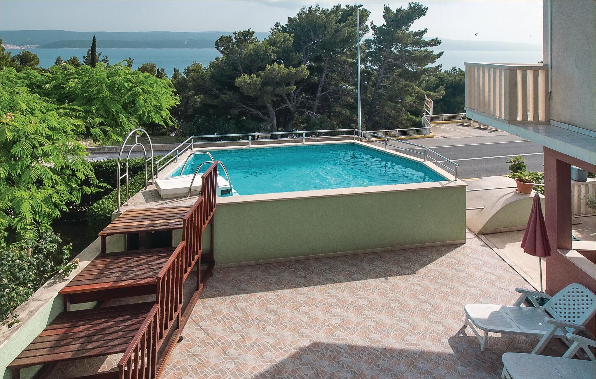 A rooftop pool with a view of the sea, surrounded by greenery and a wooden deck.