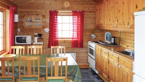 A wooden cabin with a dining area, kitchen, and a window with red curtains.