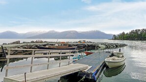 A wooden dock with boats moored at the end, a rocky shoreline, and a mountain range in the background.
