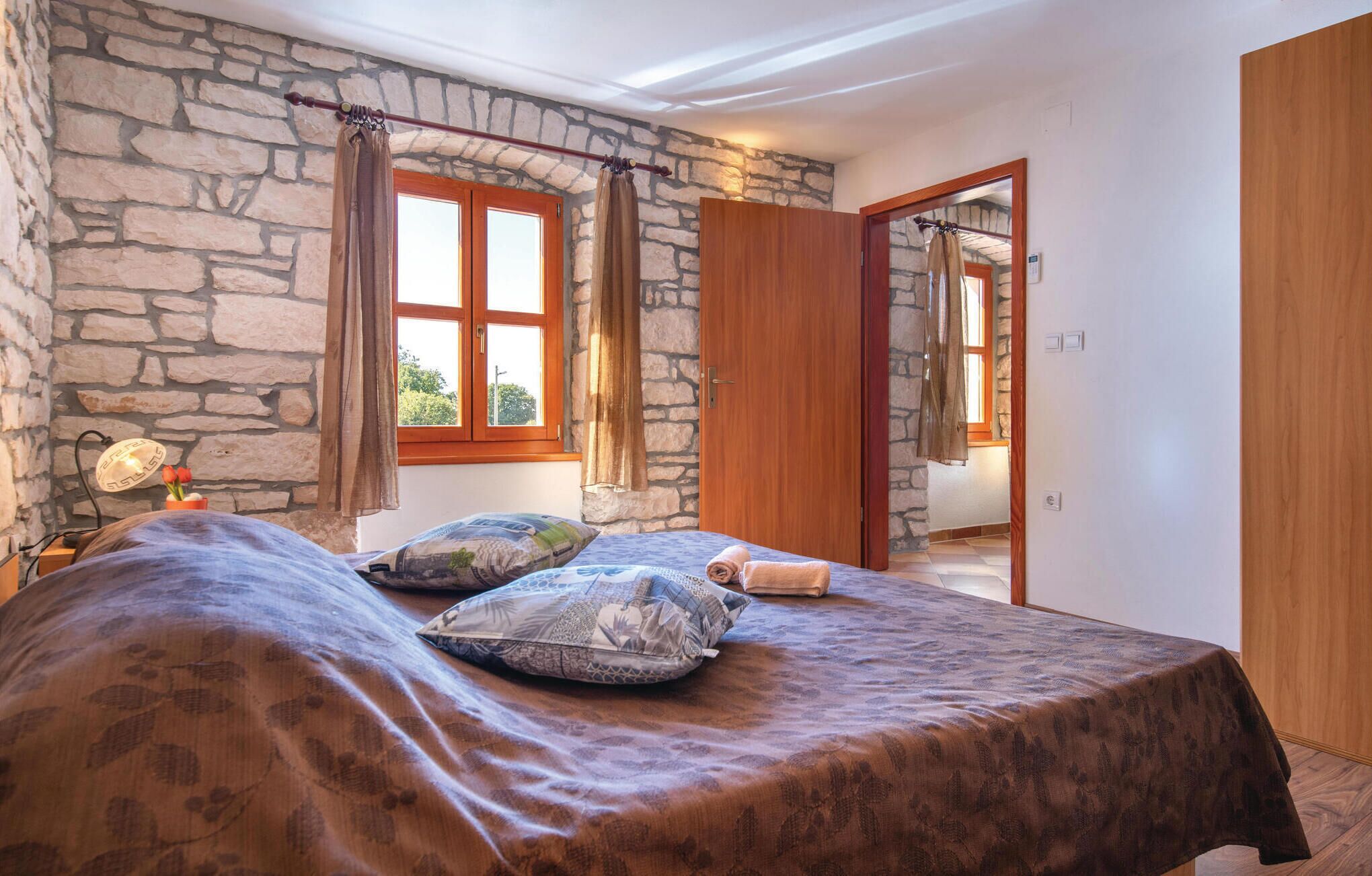 Una camera da letto con parete in pietra, porta in legno e letto con biancheria a motivi.