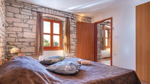 Una camera da letto con parete in pietra, porta in legno e letto con biancheria a motivi.