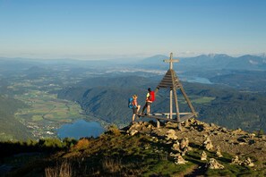 Ein Berggipfel mit einem hölzernen Kruzifix, einem See und einem Tal darunter.