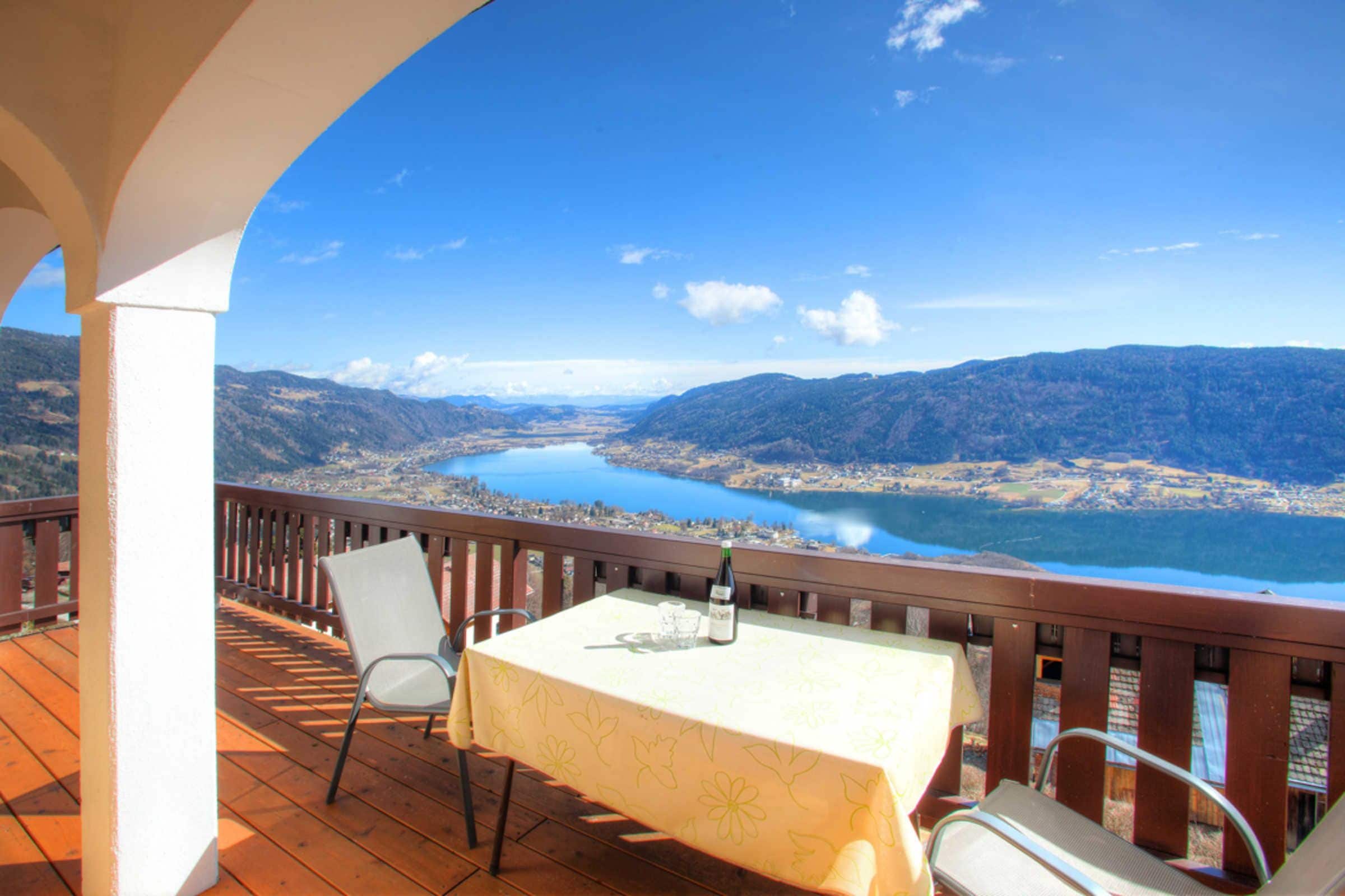 A balcony with a table and chairs, overlooking a lake and mountains.
