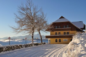 A snow-covered building with a sign reading 'Gästehaus' and a clear view of mountains in the background. - Mathiasl Panorama Apartments - Panorama Apartment (Winkl Ossiachberg)