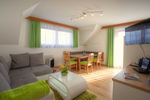 Un salon moderne comprenant un canapé, une table à manger et des chaises, un téléviseur à écran plat et un luminaire suspendu au plafond.