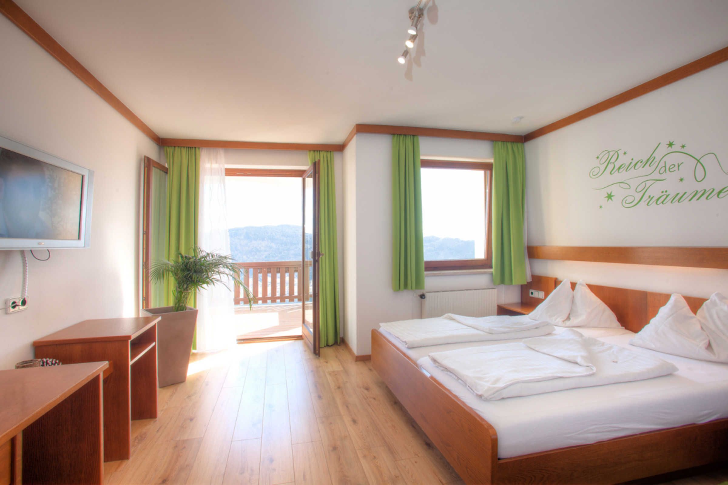 A hotel room with a wooden bed, a desk, a chair, a television, and a balcony with curtains.