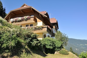 A multi-story building with balconies, surrounded by greenery and hills. - Mathiasl Panorama Apartments - Panorama Apartment (Winkl Ossiachberg)