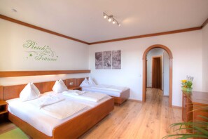 A hotel room with a large bed, a smaller bed, a wooden headboard, a wall-mounted artwork, and a hallway leading to another room. - Mathiasl Panorama Apartments - Panorama Apartment (Winkl Ossiachberg)