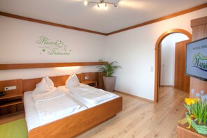 A hotel room with a wooden bed, a plant, and a TV on the wall. - Mathiasl Panorama Apartments - Panorama Apartment (Winkl Ossiachberg)