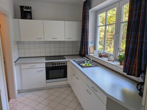 A compact kitchen with white cabinets, a built-in oven, a sink, and a window with curtains.