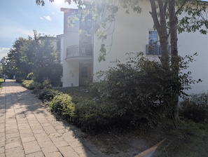 Un edificio con balcón, un sendero pavimentado y vegetación circundante.