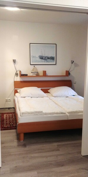 A neatly made bed with white linens, a wooden headboard, and a framed picture of a harbor on the wall.