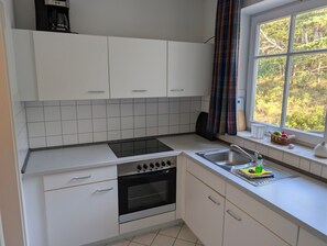 Una cocina con armarios blancos, una estufa negra, un fregadero y una ventana con vistas a árboles.