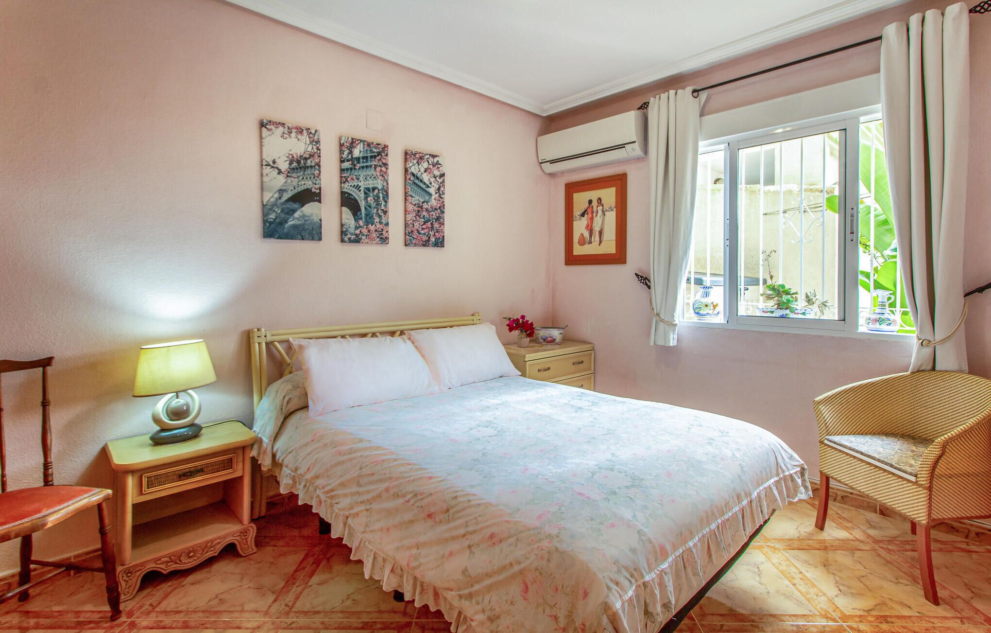 Une chambre à coucher avec un lit, une chaise, une table de chevet, une lampe et une fenêtre avec des rideaux.