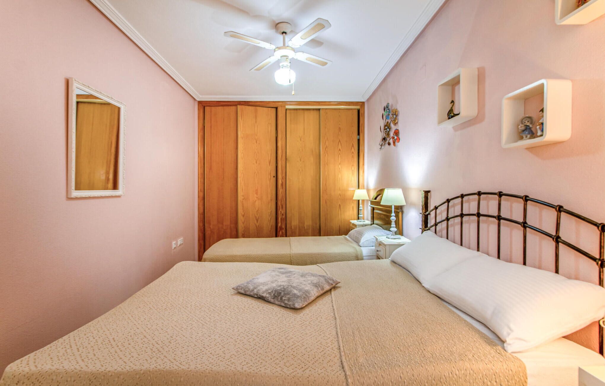 Ein Schlafzimmer mit zwei Betten, einem Deckenventilator, einem Nachttisch mit Lampe und einem Holzschrank.