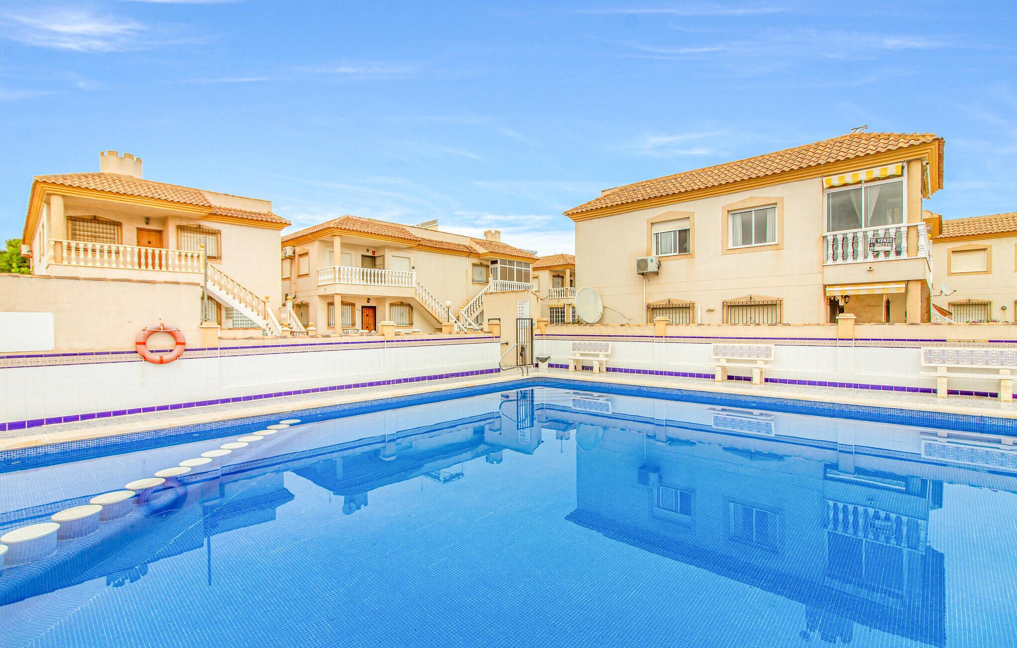 A swimming pool surrounded by buildings with balconies and a lifebuoy on the poolside.