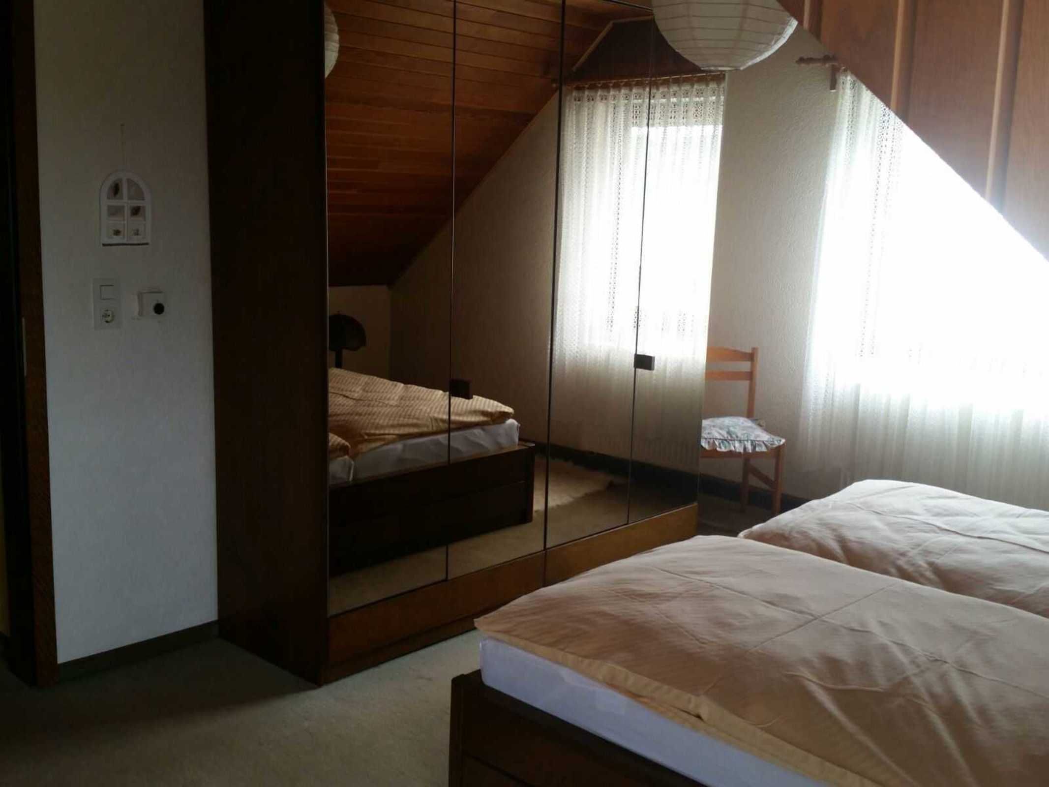 A bedroom with a sloped ceiling, a bed, a chair, and a window with curtains.