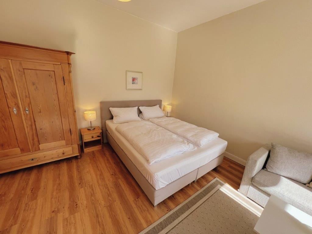 Ein Schlafzimmer mit einem Bett, einem Holzschrank, Nachttischen und einem Schlafsofa.