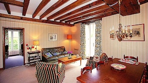 Una sala de estar con techo de madera, un sofá, una mesa de comedor con sillas, una lámpara de araña y una ventana con cortinas.
