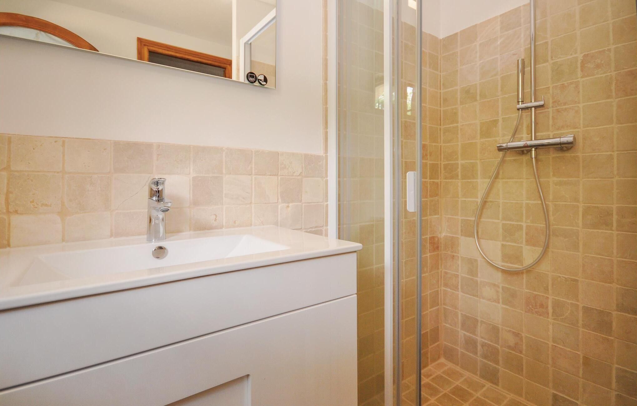 A bathroom with a glass-enclosed shower, a white sink, and beige tiled walls.