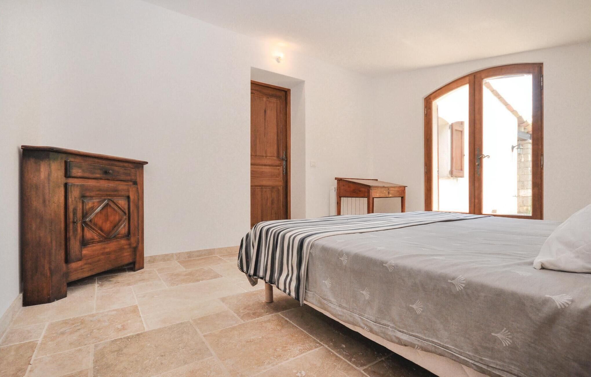 Une chambre à coucher avec un lit, une commode en bois, une petite table et une fenêtre donnant sur un beau paysage.