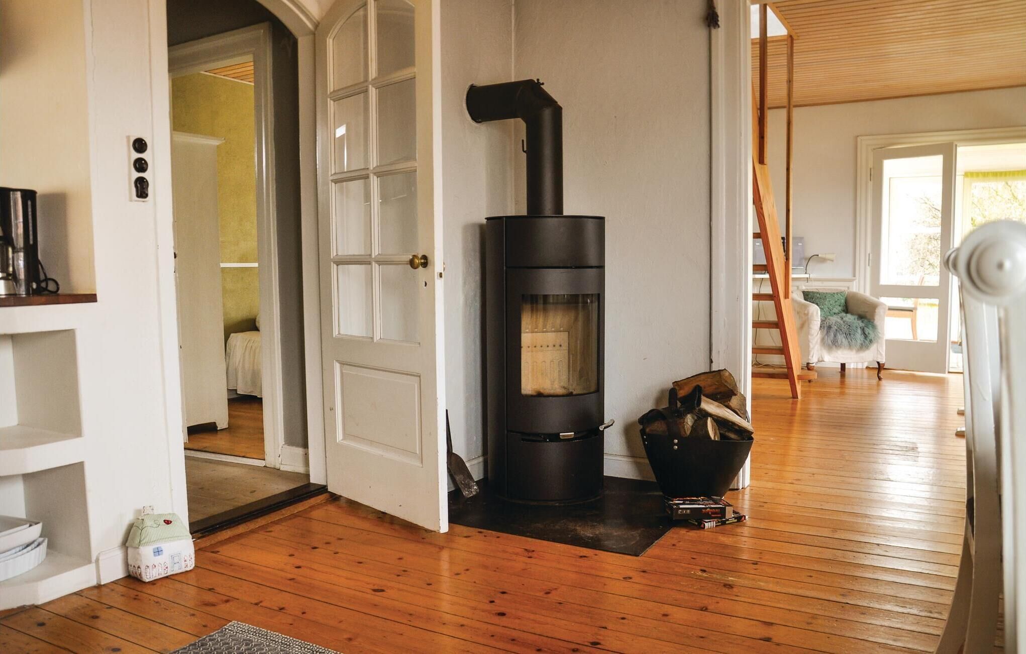 Une pièce chaleureuse avec un poêle à bois, un plancher en bois et une porte blanche donnant sur une autre pièce.
