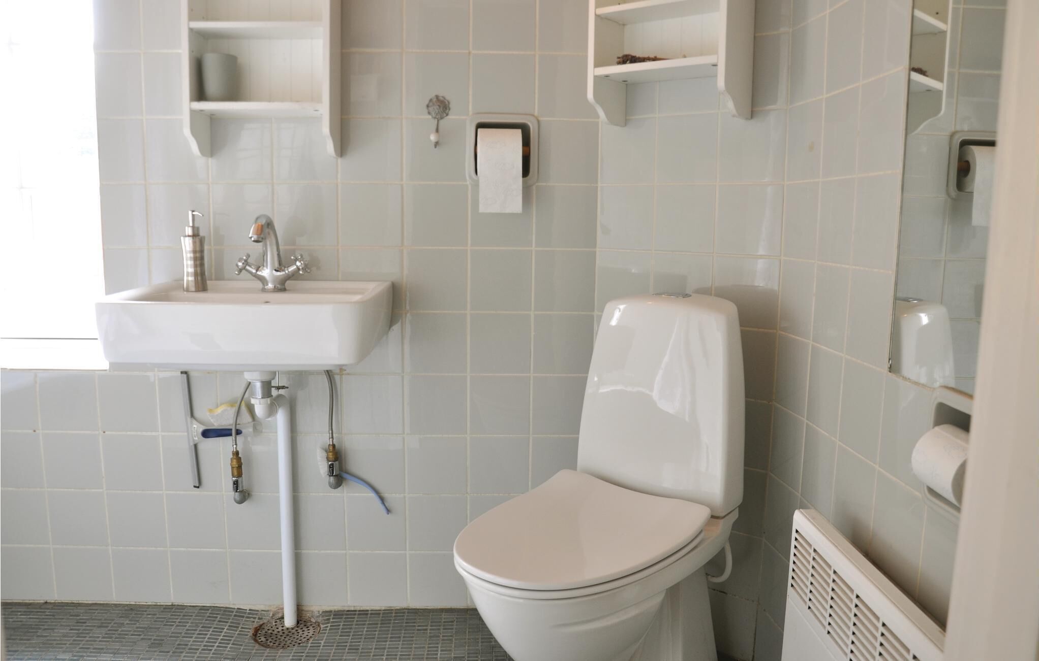 A bathroom with a white sink, toilet, and a towel dispenser.
