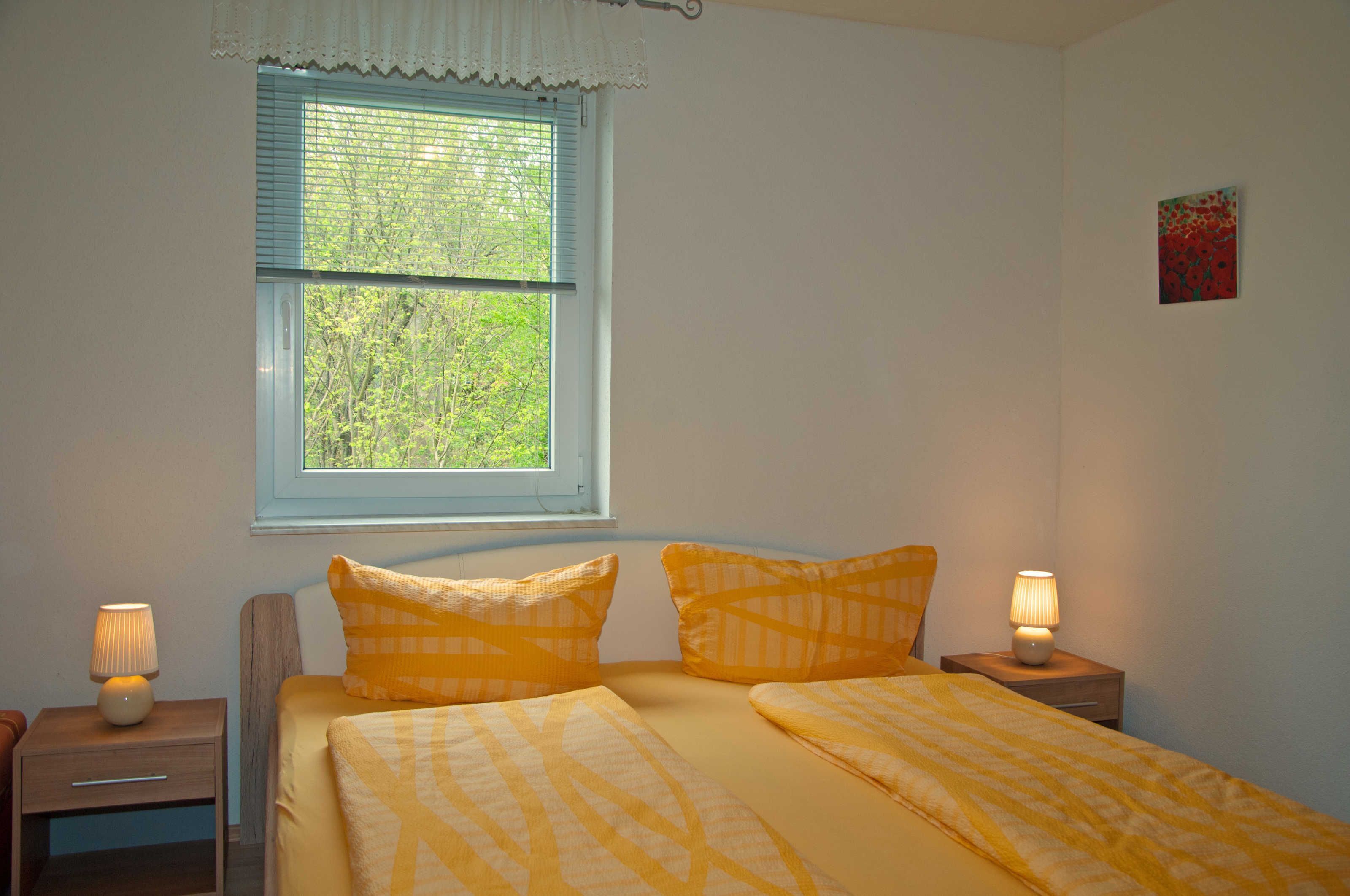 Ein Schlafzimmer mit einem Bett, zwei Nachttischen, einem Fenster mit Jalousien und einem Wandbild.