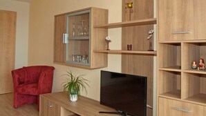 A living room with a TV, wooden shelves, a red chair, and a potted plant. - Strandkorbhaus 9 150 m to the beach quiet location - Strandkorbhaus 9 150 m to the beach (Göhren)